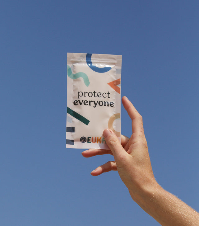 Hand holding up Euka Sanitizing Wipes package against a blue sky